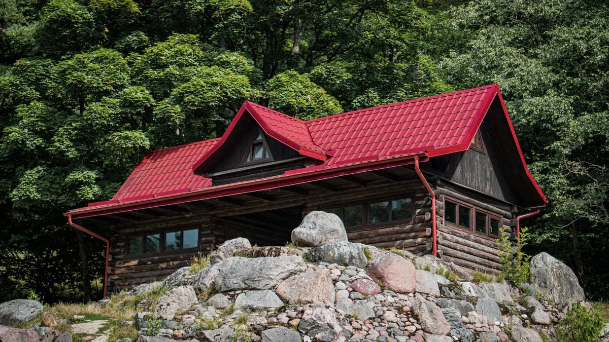 Charming wooden cabin with a red roof nestled among trees and rocks, ideal for nature retreats.